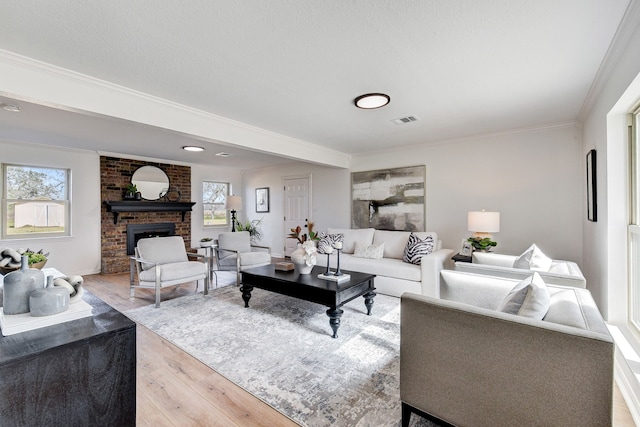 living room with wood-type flooring, a brick fireplace, ornamental molding, and a textured ceiling