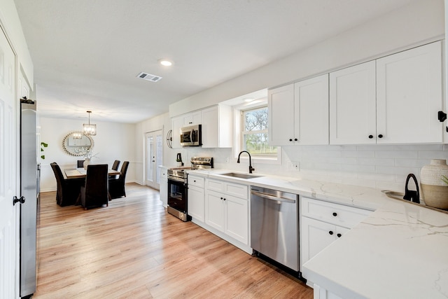 kitchen with appliances with stainless steel finishes, white cabinetry, sink, hanging light fixtures, and light hardwood / wood-style floors