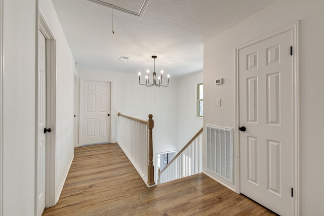 hallway with a chandelier, light hardwood / wood-style flooring, and a textured ceiling