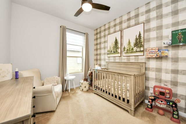 bedroom featuring a nursery area, ceiling fan, and carpet