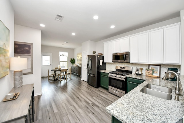 kitchen with sink, white cabinetry, hanging light fixtures, appliances with stainless steel finishes, and backsplash