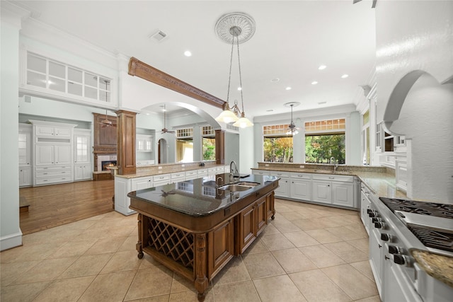 kitchen with white cabinetry, crown molding, range, a center island with sink, and pendant lighting