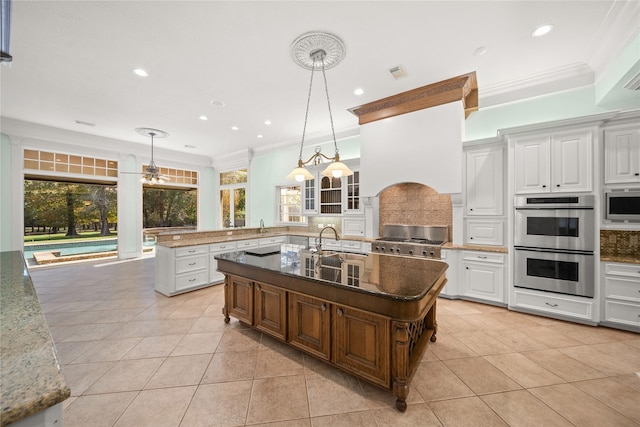 kitchen with hanging light fixtures, an island with sink, white cabinets, and stainless steel appliances