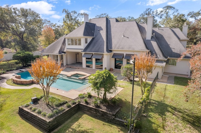 back of house featuring a swimming pool with hot tub, a patio, and a lawn