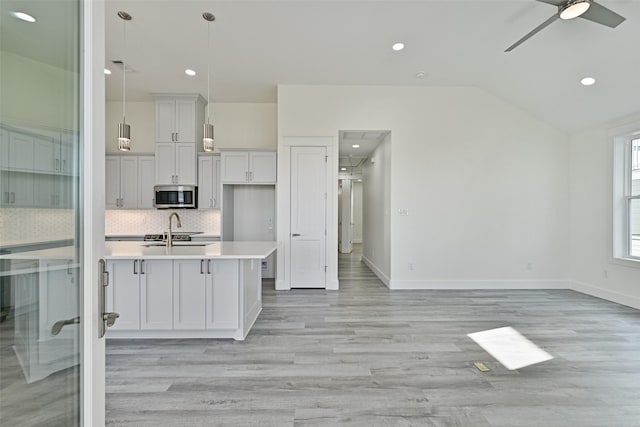 kitchen with sink, vaulted ceiling, hanging light fixtures, light wood-type flooring, and backsplash