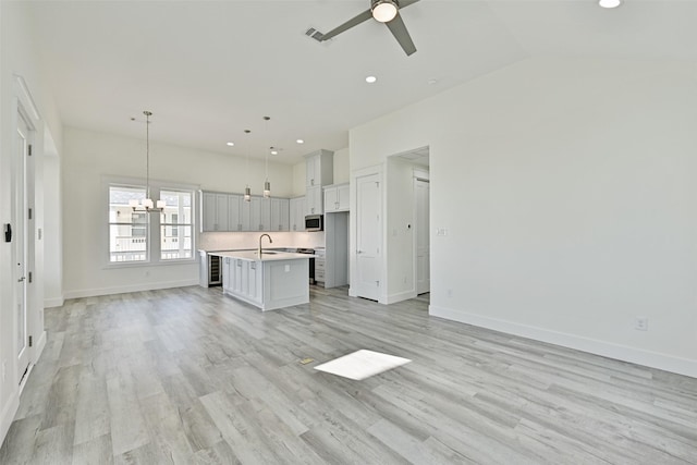 unfurnished living room with sink, ceiling fan with notable chandelier, vaulted ceiling, and light wood-type flooring