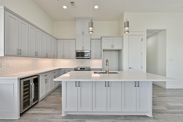 kitchen featuring sink, decorative light fixtures, a center island with sink, stainless steel appliances, and beverage cooler