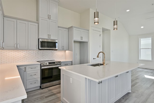 kitchen featuring sink, light stone counters, an island with sink, pendant lighting, and stainless steel appliances