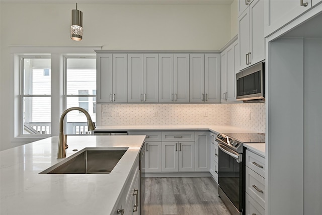 kitchen with sink, light stone counters, pendant lighting, stainless steel appliances, and decorative backsplash