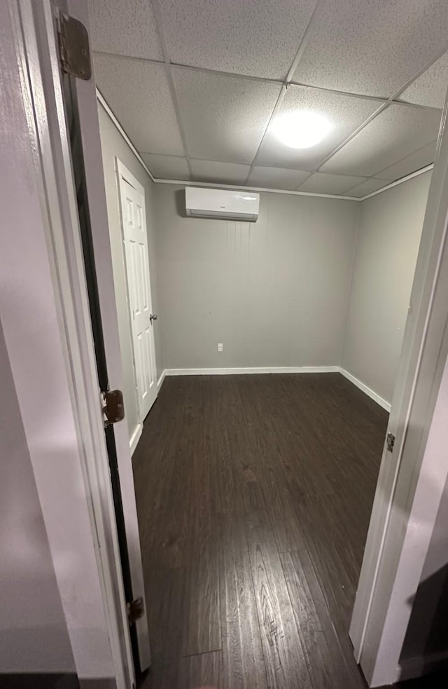 basement with a wall mounted air conditioner, a drop ceiling, and dark hardwood / wood-style flooring