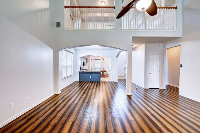 unfurnished living room featuring dark hardwood / wood-style flooring, a towering ceiling, and ceiling fan