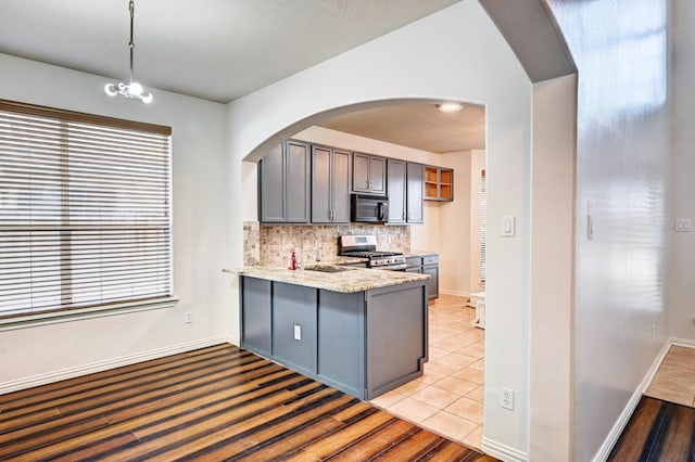 kitchen featuring sink, stainless steel gas range oven, decorative light fixtures, kitchen peninsula, and backsplash