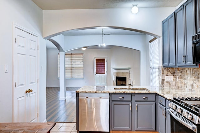 kitchen featuring sink, tasteful backsplash, light stone counters, gray cabinets, and stainless steel appliances