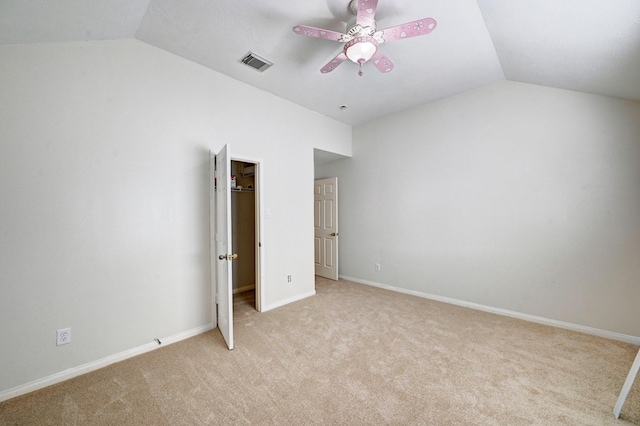 unfurnished bedroom with lofted ceiling, a walk in closet, light colored carpet, a closet, and ceiling fan