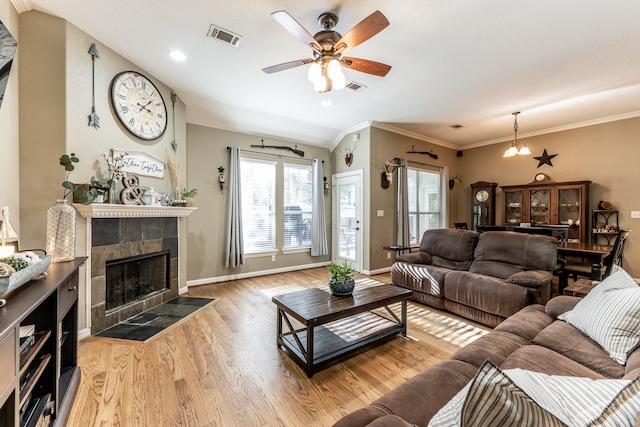 living room featuring ceiling fan, ornamental molding, a tiled fireplace, and light hardwood / wood-style floors