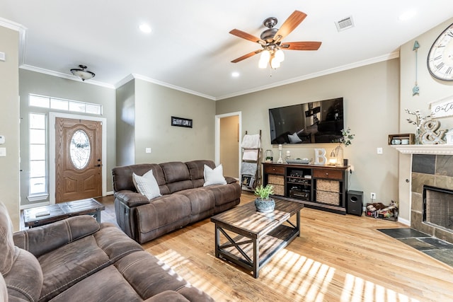 living room featuring crown molding, a tile fireplace, ceiling fan, and light wood-type flooring