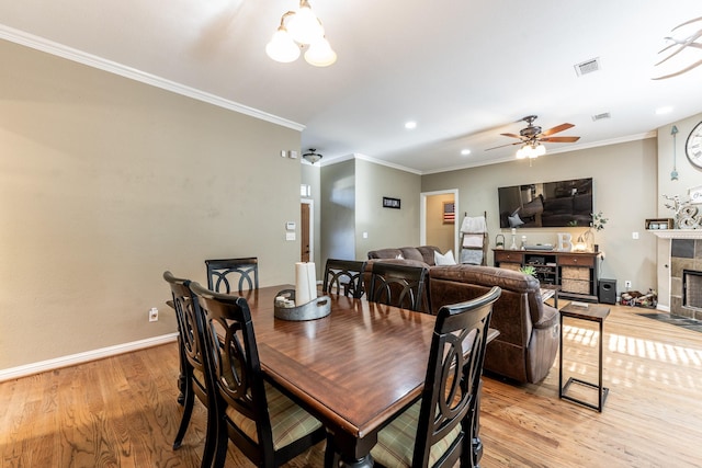 dining area with crown molding, a fireplace, ceiling fan with notable chandelier, and light hardwood / wood-style floors