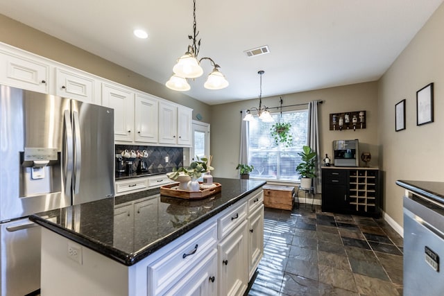 kitchen featuring decorative light fixtures, white cabinets, stainless steel fridge, dark stone counters, and a center island