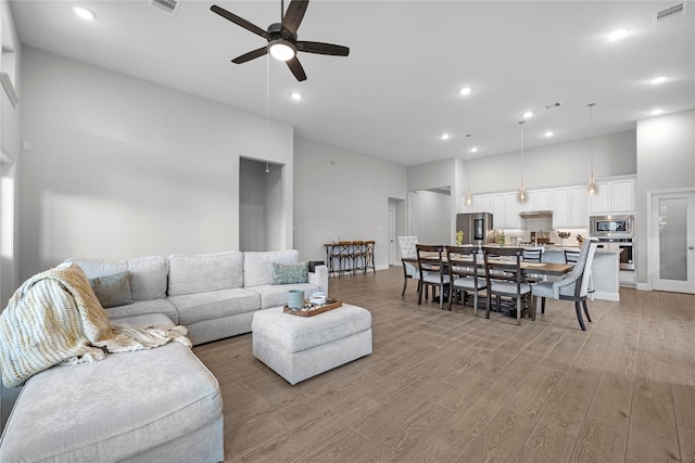 living room with a high ceiling, ceiling fan, and light hardwood / wood-style floors