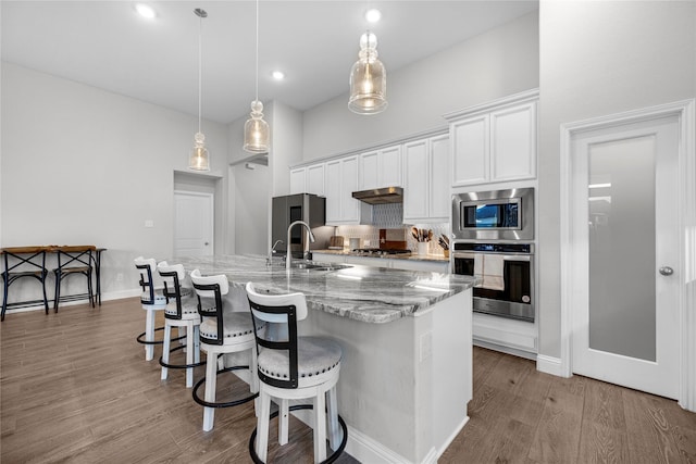 kitchen with sink, hanging light fixtures, appliances with stainless steel finishes, a kitchen island with sink, and white cabinets