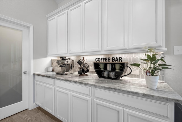 bar with light stone countertops, decorative backsplash, and white cabinets