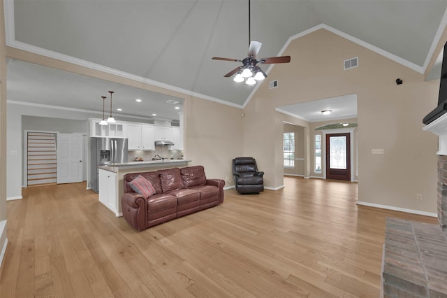 living room with ornamental molding, a brick fireplace, high vaulted ceiling, and light hardwood / wood-style flooring