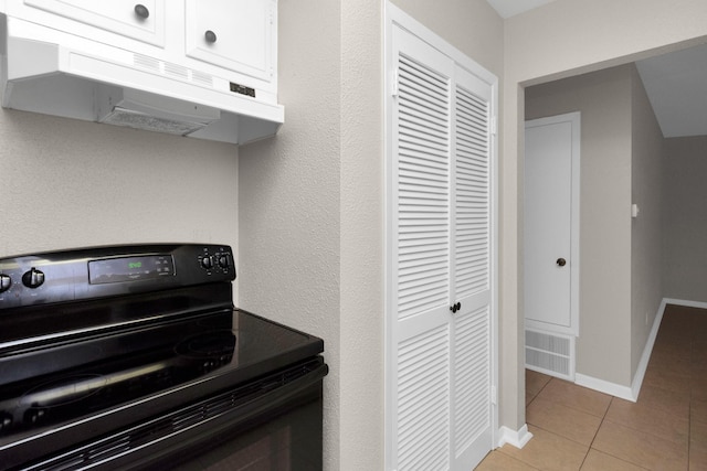 kitchen featuring electric range, white cabinets, and light tile patterned flooring