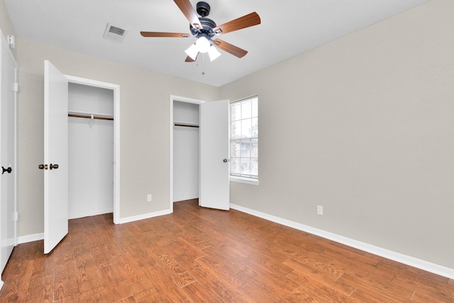 unfurnished bedroom featuring multiple closets, wood-type flooring, and ceiling fan