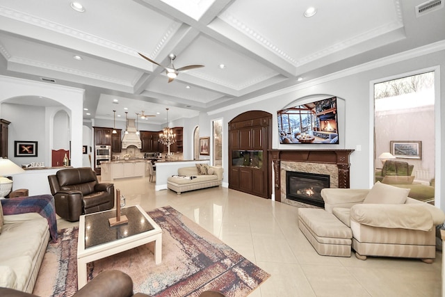 tiled living room with crown molding, beam ceiling, coffered ceiling, a high end fireplace, and ceiling fan with notable chandelier