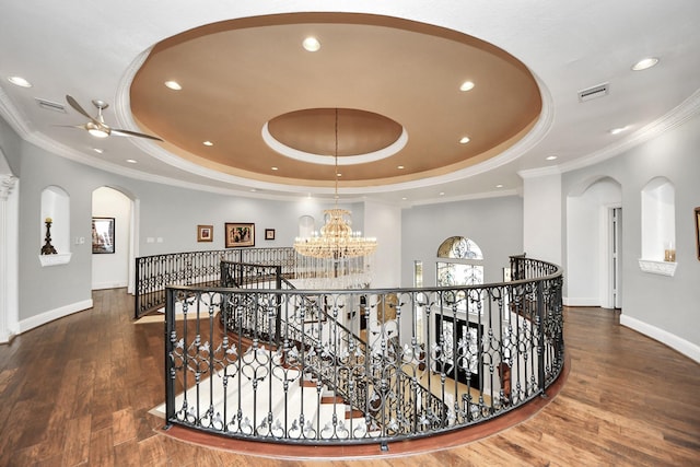 hallway featuring an inviting chandelier, a tray ceiling, dark wood-type flooring, and ornamental molding