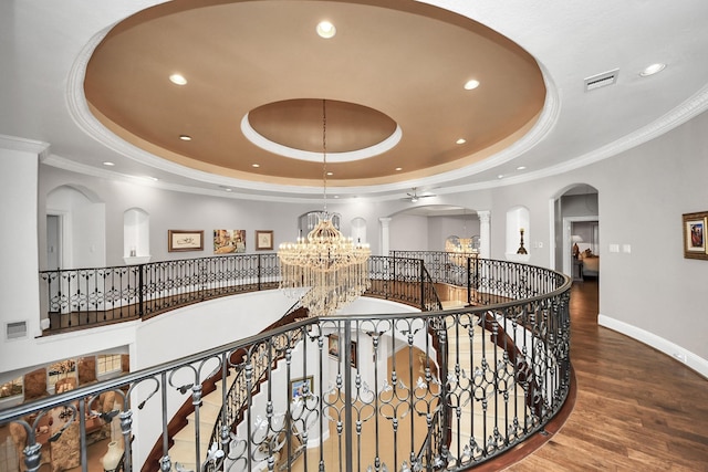 hallway featuring crown molding, an inviting chandelier, hardwood / wood-style floors, a raised ceiling, and ornate columns