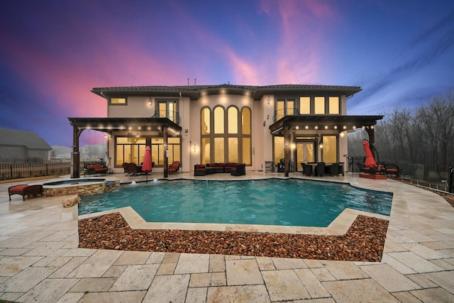 back house at dusk featuring a pool with hot tub and a patio area