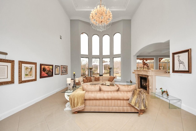 tiled living room with crown molding, a tile fireplace, a towering ceiling, a raised ceiling, and a chandelier