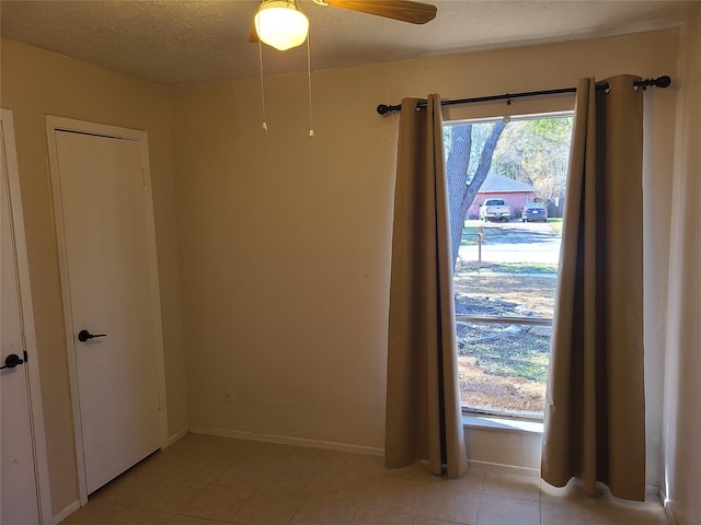 spare room featuring ceiling fan, light tile patterned floors, and a textured ceiling