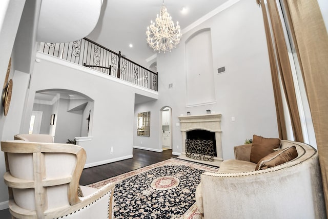 living room featuring dark wood-type flooring, crown molding, a chandelier, a towering ceiling, and a high end fireplace