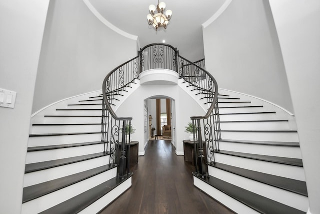 entryway with an inviting chandelier, a towering ceiling, ornamental molding, and dark hardwood / wood-style flooring