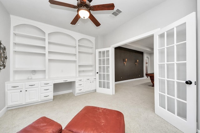 interior space featuring built in desk, light colored carpet, french doors, and ceiling fan