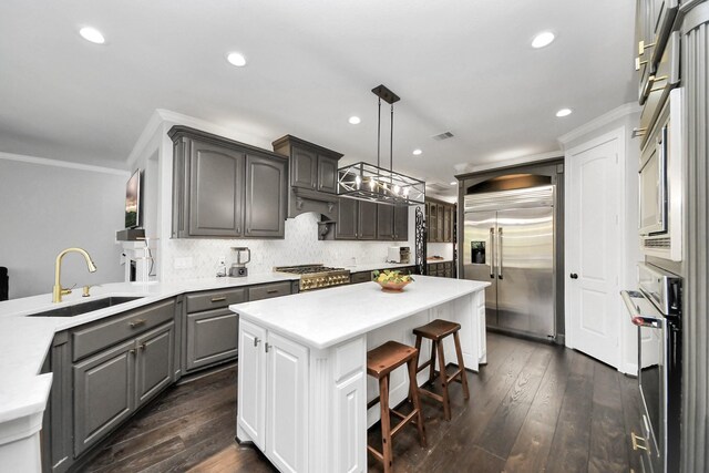 kitchen with pendant lighting, sink, stainless steel appliances, ornamental molding, and decorative backsplash