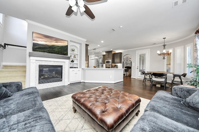 living room featuring ceiling fan with notable chandelier, dark wood-type flooring, ornamental molding, and a premium fireplace