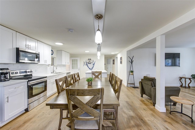 kitchen featuring sink, white cabinetry, stainless steel appliances, tasteful backsplash, and decorative light fixtures