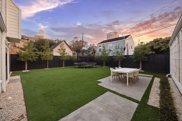 yard at dusk featuring a patio area and a trampoline