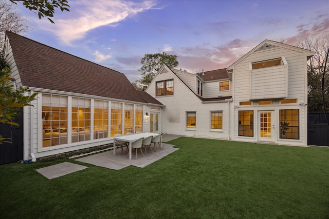 back house at dusk with a patio area, french doors, and a lawn