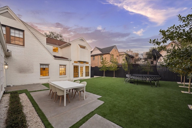 yard at dusk featuring french doors, a trampoline, and a patio area