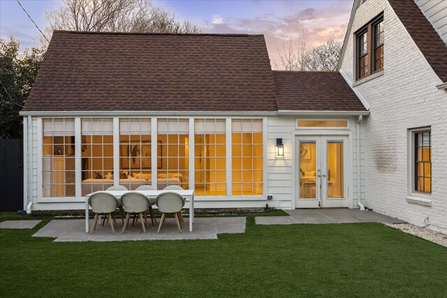 back house at dusk featuring a lawn and a patio area