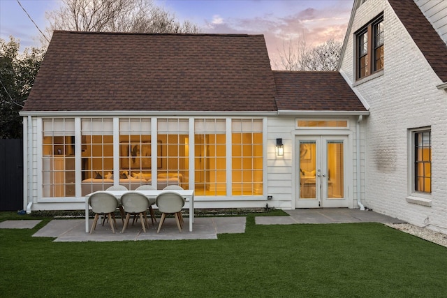 back house at dusk with a patio and a lawn