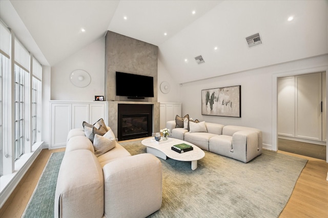 living room featuring high vaulted ceiling, a fireplace, and light hardwood / wood-style floors