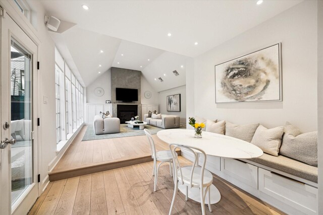 dining area featuring breakfast area, a large fireplace, lofted ceiling, and light hardwood / wood-style floors