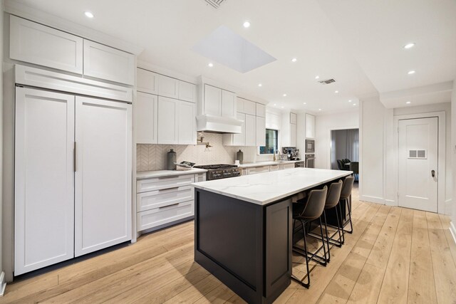 kitchen with light stone counters, built in appliances, custom range hood, and white cabinets