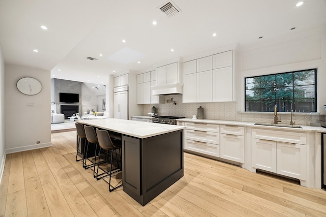 kitchen with sink, a center island, white cabinets, light stone countertops, and backsplash