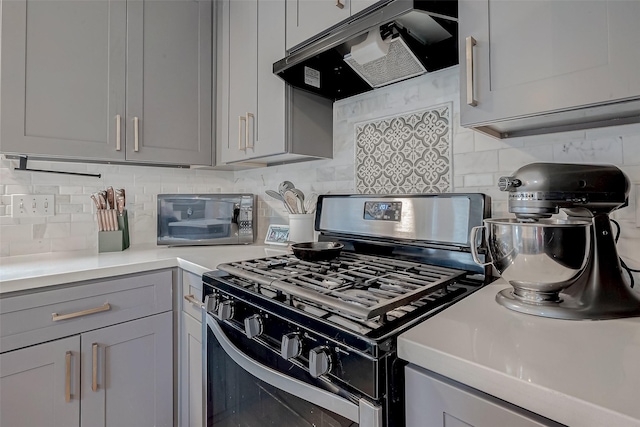 kitchen featuring ventilation hood, gray cabinets, backsplash, and range with gas cooktop